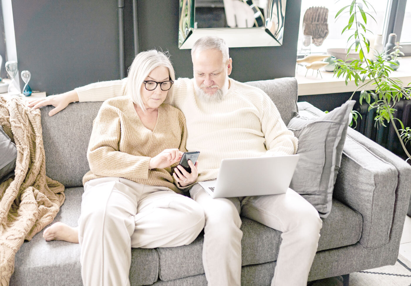 Pärchen ab 50 auf dem Sofa mit Smartphone und Laptop